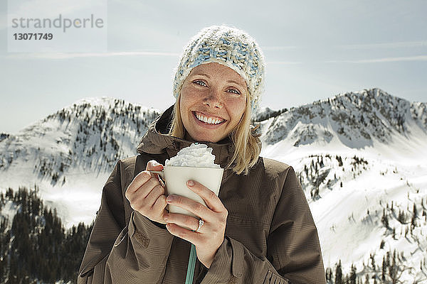 Porträt einer Frau  die Schlagsahne hält  während sie gegen einen schneebedeckten Berg steht