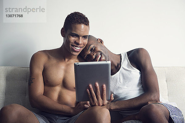 Schwules Paar betrachtet Tablet-Computer  während es auf dem Sofa sitzt