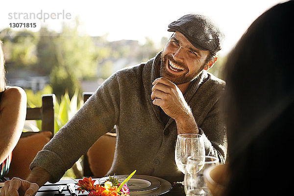 Fröhlicher Mann schaut weg  während er mit Freunden am Esstisch sitzt