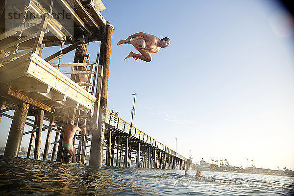 Mann springt von Pier im Meer gegen klaren Himmel