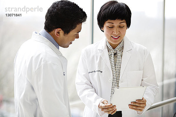 Glückliche Ärzte schauen auf Tablet-Computer  während sie im Krankenhaus stehen