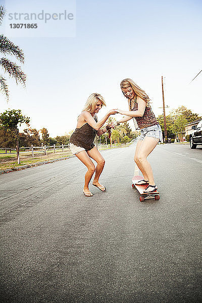 Freunde spielen mit dem Skateboard auf der Straße gegen den klaren Himmel