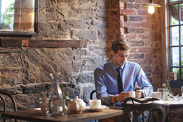 Mann benutzt Mobiltelefon  während er im Café sitzt