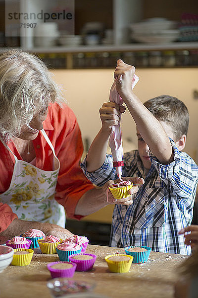 Junge mit Großmutter füllt Cupcake-Halter in der Küche