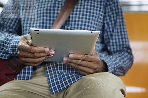Mittelsektion eines Mannes  der einen Tablet-Computer benutzt  während er im Zug reist