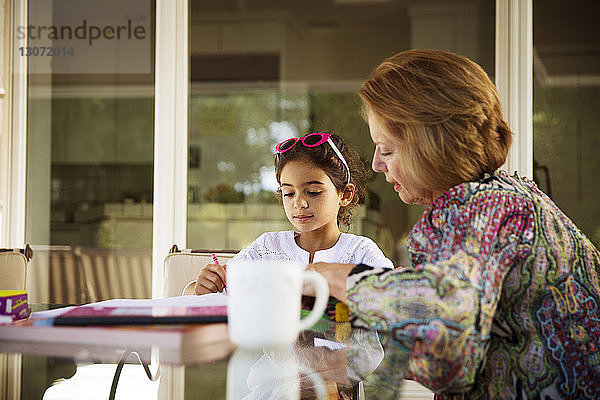 Großmutter hilft Enkelin beim Lernen am Tisch