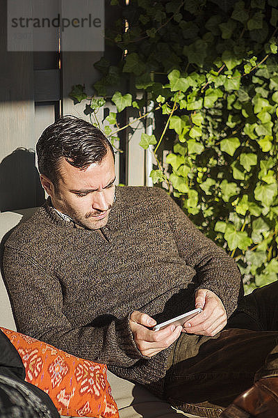 Mann benutzt Smartphone  während er auf der Couch im Hof liegt