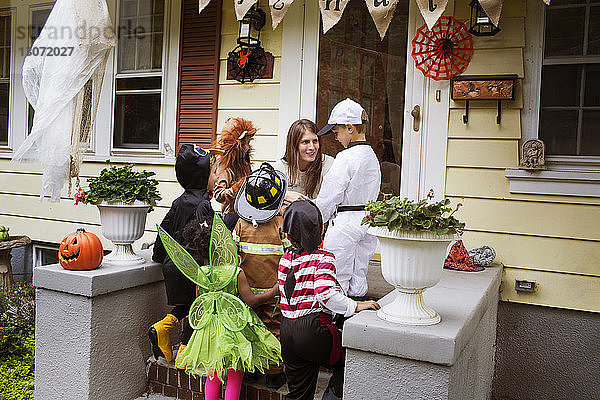 Frau spricht mit Kindern in Halloween-Kostümen während eines Streiches oder einer Behandlung