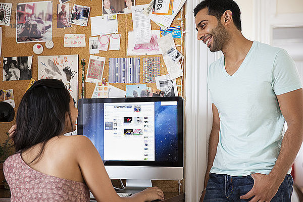 Mann sieht Frau an  die zu Hause einen Desktop-Computer benutzt