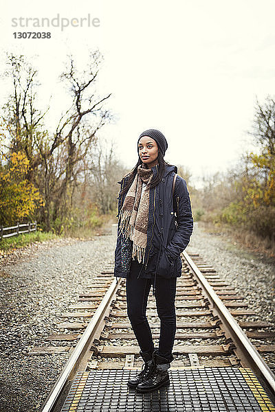 Nachdenkliche Frau steht auf Eisenbahnschienen vor klarem Himmel