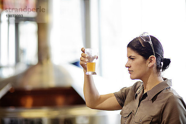 Frau untersucht Bier im Glasbecher  während sie in der Brauerei steht