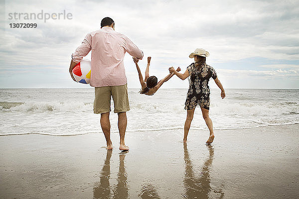 Rückansicht von spielerischen Eltern  die ihre Tochter am Strand aussuchen