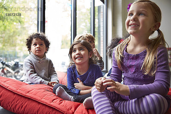 Lächelnde Kinder entspannen sich in der Vorschule auf einer Decke am Fenster