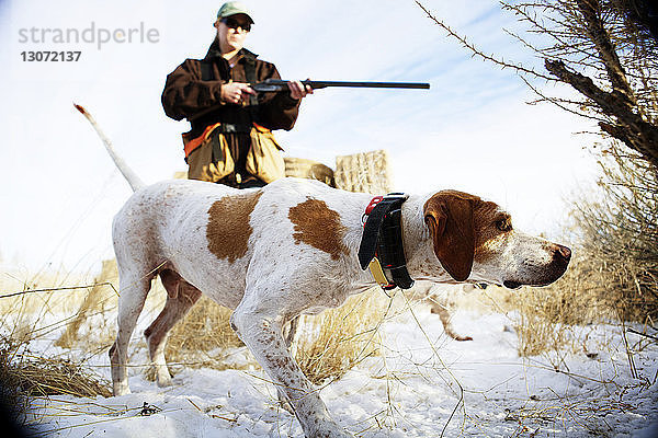 Frau hält Gewehr  während sie mit Hund auf schneebedecktem Feld steht