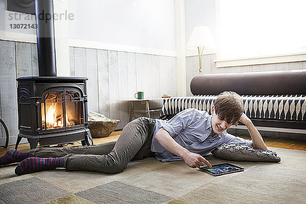 Mann benutzt Tablet-Computer  während er zu Hause auf dem Boden liegt