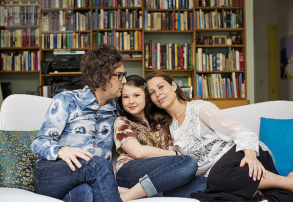 Mädchen mit Eltern  die zu Hause auf dem Sofa sitzen