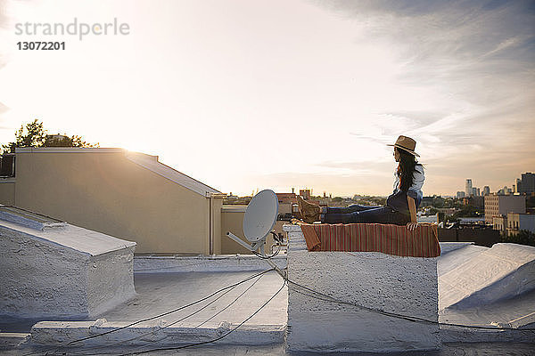 Seitenansicht einer Frau  die auf einer Gebäudeterrasse gegen den Himmel sitzt