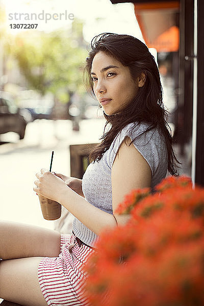 Nachdenkliche Frau trinkt Kaffee  während sie in einem Straßencafé in der Stadt sitzt