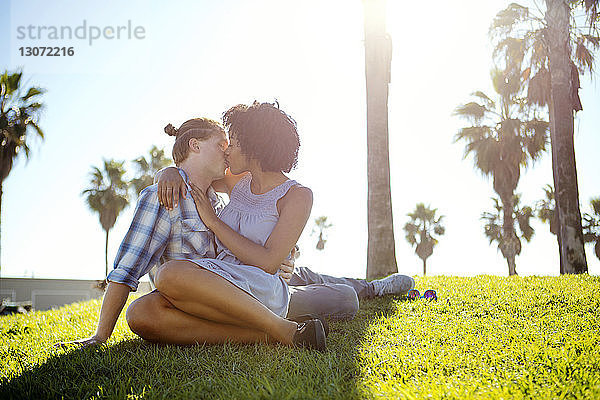 Zärtliches Paar küsst sich beim Sitzen auf dem Feld gegen den Himmel