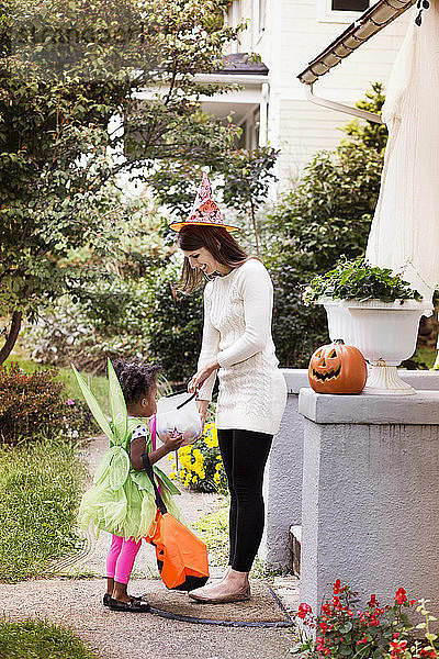 Frau verschenkt Süßigkeiten an Mädchen in Halloween-Kostüm während Trick oder Behandlung