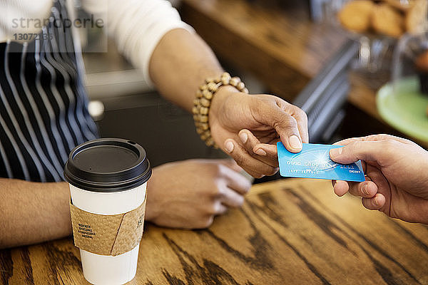 Schrägaufnahme eines Mannes  der dem Besitzer im Café eine Debitkarte gibt