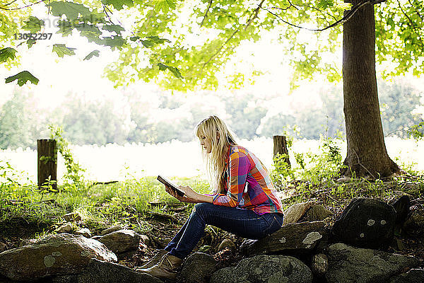 Seitenansicht einer Frau  die auf dem Feld sitzend ein Buch liest
