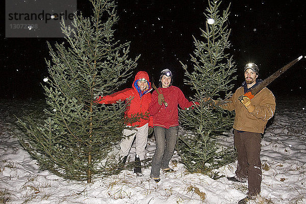 Glückliche Freunde halten Werkzeuge in der Hand und stehen inmitten von Bäumen auf einem schneebedeckten Feld