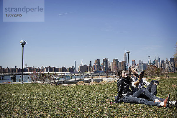 Fröhliches Paar telefoniert mit dem Handy und entspannt sich auf dem Feld vor blauem Himmel