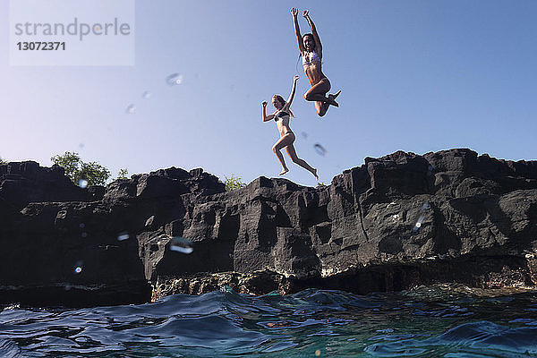 Freunde springen von der Klippe ins Meer