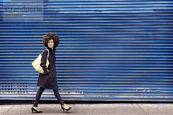Lächelnde Frau in voller Länge mit blauem Fensterladen auf dem Bürgersteig