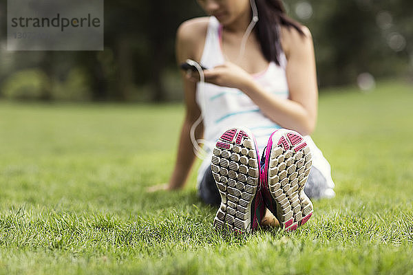 Niedriger Teil einer Frau  die ein Smartphone benutzt  während sie auf einem Grasfeld im Park sitzt