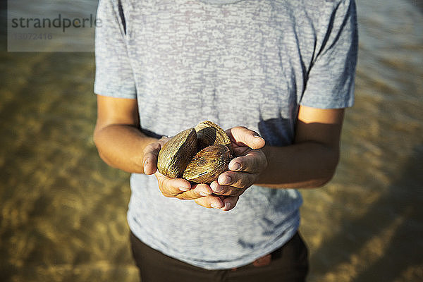 Ein Mann hält Muscheln  während er am Meeresufer steht