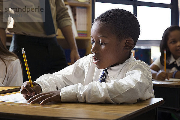 Junge schreibt während des Unterrichts im Klassenzimmer auf Papier