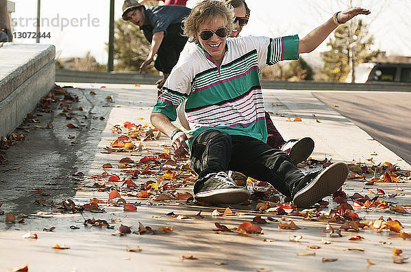 Fröhliche Freunde sitzen auf Skateboard  während sie im Park rutschen