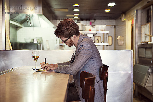 Seitenansicht eines Mannes  der schreibt  während er am Tisch im Restaurant sitzt