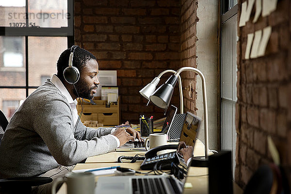 Seitenansicht eines Geschäftsmannes  der während seiner Arbeit im Büro Musik hört