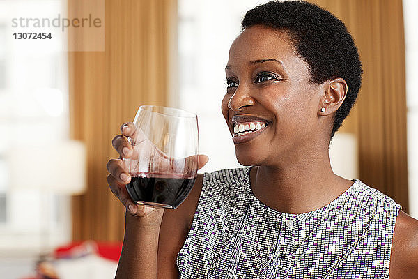 Glückliche Frau schaut weg  während sie zu Hause Weinglas hält