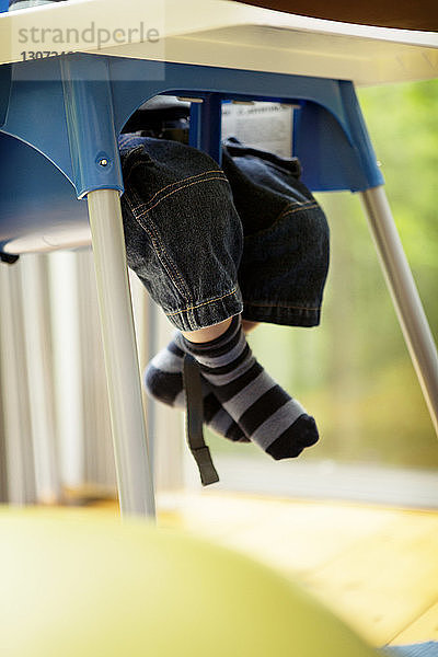 Niedriger Teil eines Jungen  der zu Hause auf einem Hochstuhl sitzt