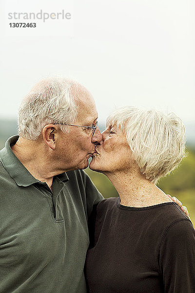 Zärtliches Seniorenpaar küsst sich im Stehen gegen den Himmel