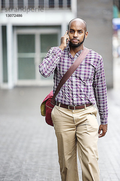 Mann spricht mit Smartphone  während er in der Stadt auf der Straße geht