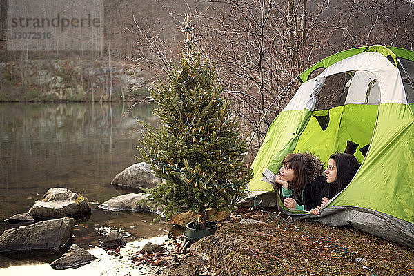 Freunde schauen weg  während sie im Zelt am Weihnachtsbaum liegen