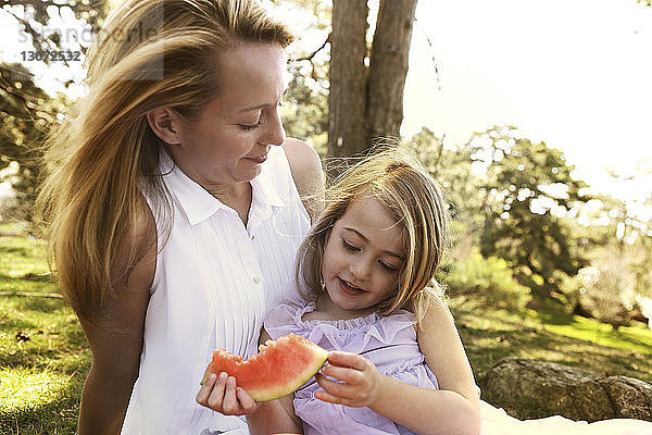 Mutter betrachtet Mädchen mit Wassermelone im Garten