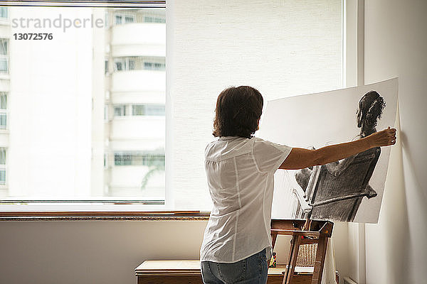 Rückansicht einer Frau  die im Kunstatelier ein Gemälde auf die Staffelei stellt