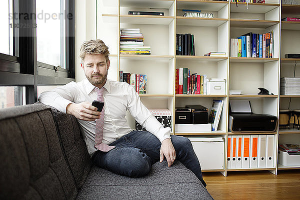 Mann benutzt Mobiltelefon  während er zu Hause auf dem Sofa sitzt