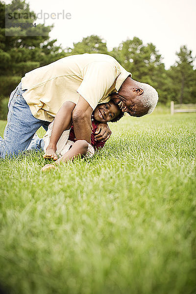 Grossvater umarmt Enkel  der auf einem Grasfeld im Hinterhof sitzt