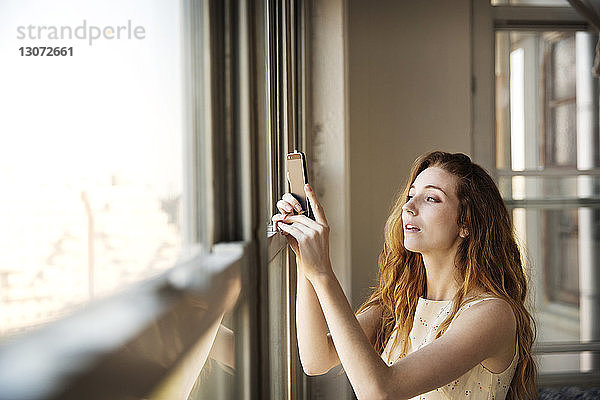 Frau fotografiert  während sie zu Hause am Fenster steht