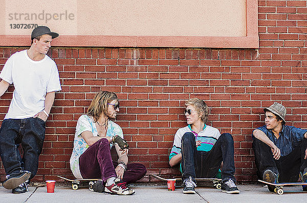 Freunde mit Skateboard reden  während sie an einer Ziegelmauer sitzen