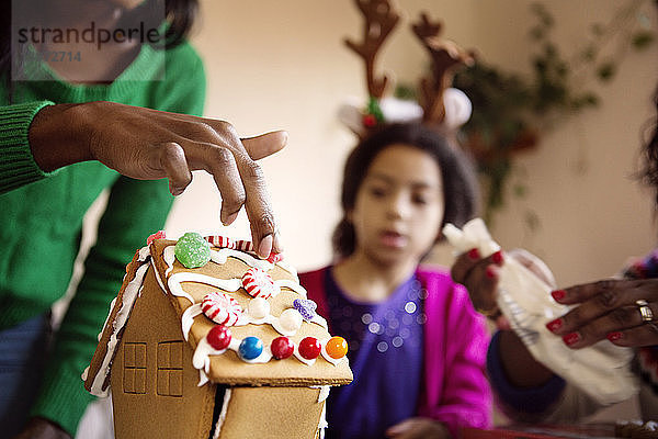 Mädchen sieht Mutter beim Dekorieren des Lebkuchenhauses zu Hause