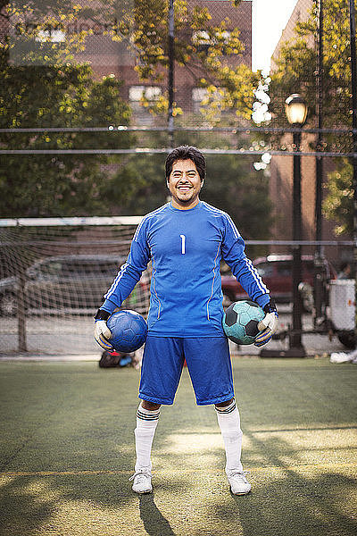 Porträt eines glücklichen Fußballspielers  der Bälle trägt  während er auf dem Spielfeld steht