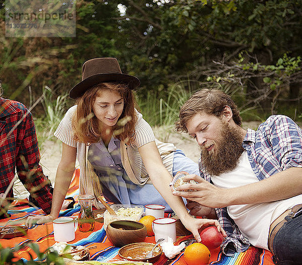 Freunde beim Frühstück  während sie sich auf einem Feld im Wald entspannen